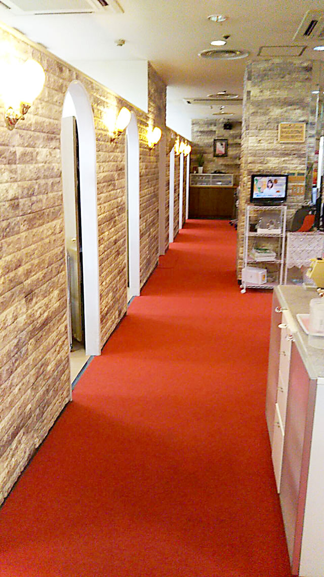 際ビル店の店内廊下の写真。赤絨毯が敷かれ、各室を区切る壁面にはブロック調の装飾が施されている。
